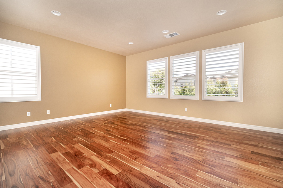 Spacious empty room with polished hardwood floors and bright windows illuminating the space.